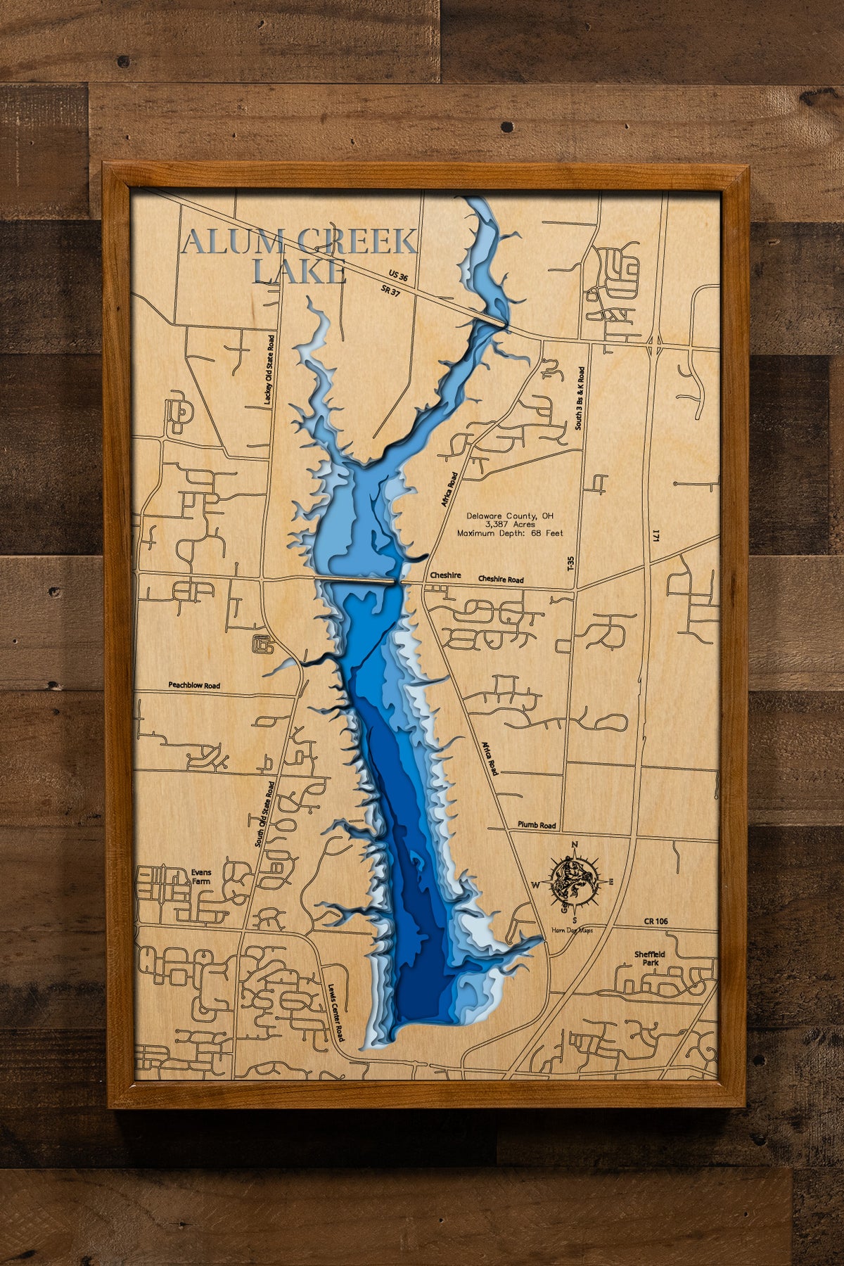 A detailed, laser-cut wooden map of Alum Creek Lake in Delaware County, Ohio, showcasing the reservoir's 3,387 acres and irregular shoreline. The map illustrates the division between the unlimited-horsepower southern basin and the quieter northern coves, with etched lines highlighting the maximum 68-foot depth near the dam structure.