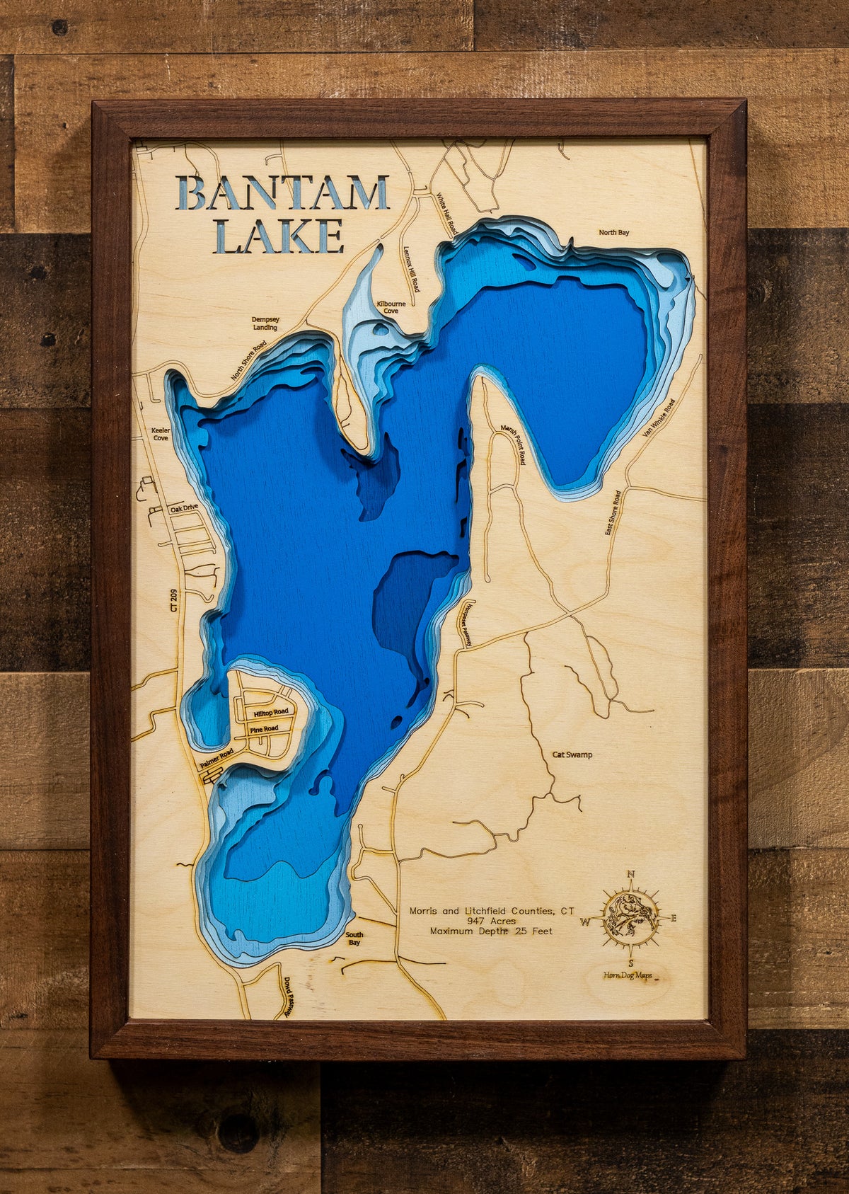 A laser-cut, layered wooden map of Bantam Lake, located in Morris and Litchfield Counties, Connecticut. The shape of Connecticut's largest natural lake is clearly defined within the northwestern Connecticut landscape. The varying depths of the lake, reaching a maximum of 25 feet, are represented by different layers of wood.