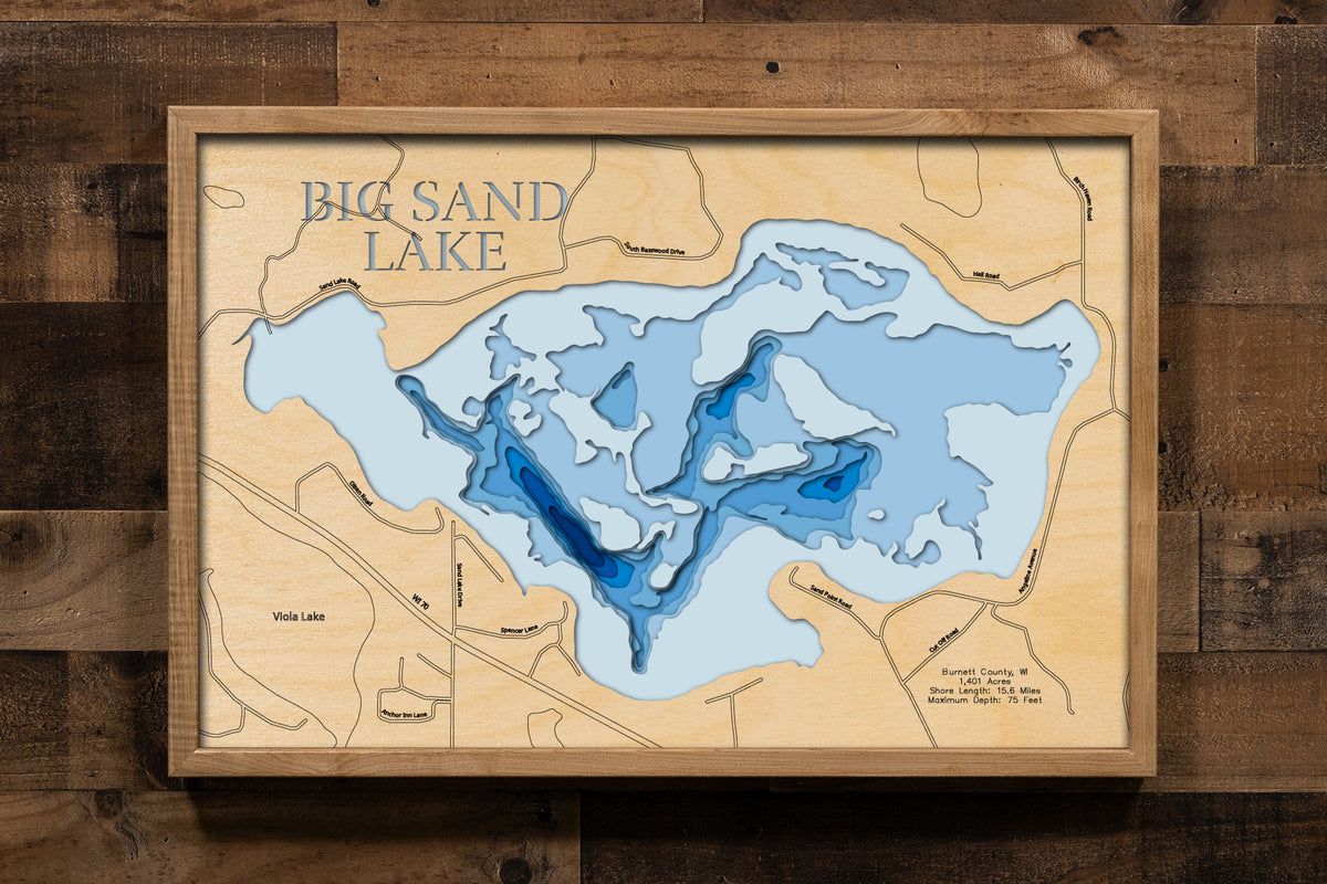 A laser-cut, layered wooden map of Big Sand Lake in Burnett County, Wisconsin. The shape of this significant natural lake, with its extensive shoreline, is visible within the northern Wisconsin landscape. The varying depths of the lake, reaching a maximum of 75 feet, are represented by different layers of wood, illustrating its underwater topography.