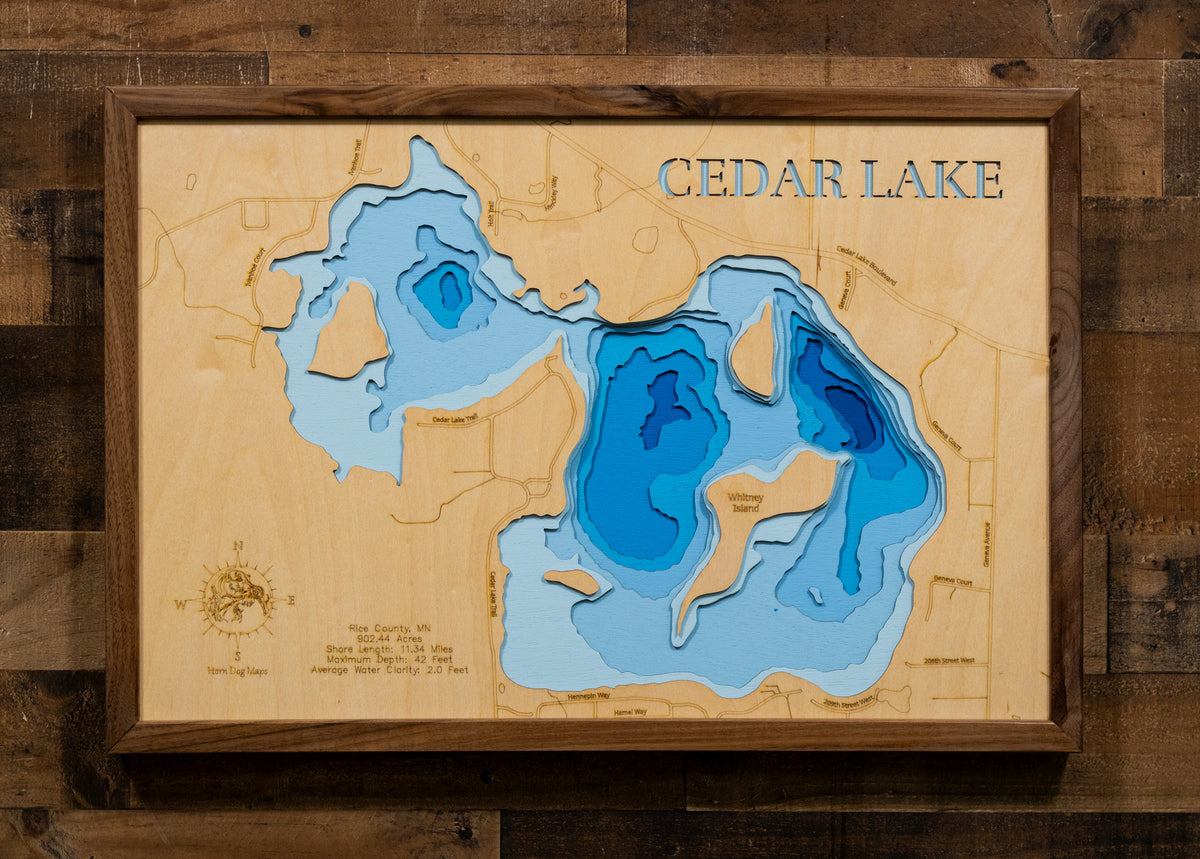 A precision laser-cut, multi-layered wooden map of Cedar Lake in Rice County, Minnesota. The natural wood top layer captures over 11 miles of shoreline and four distinctive islands in fine detail, while a light-to-dark blue gradient conveys the lake's 42-foot depth. A handcrafted statement piece for any southern Minnesota lake home, cabin, or fishing enthusiast's wall.