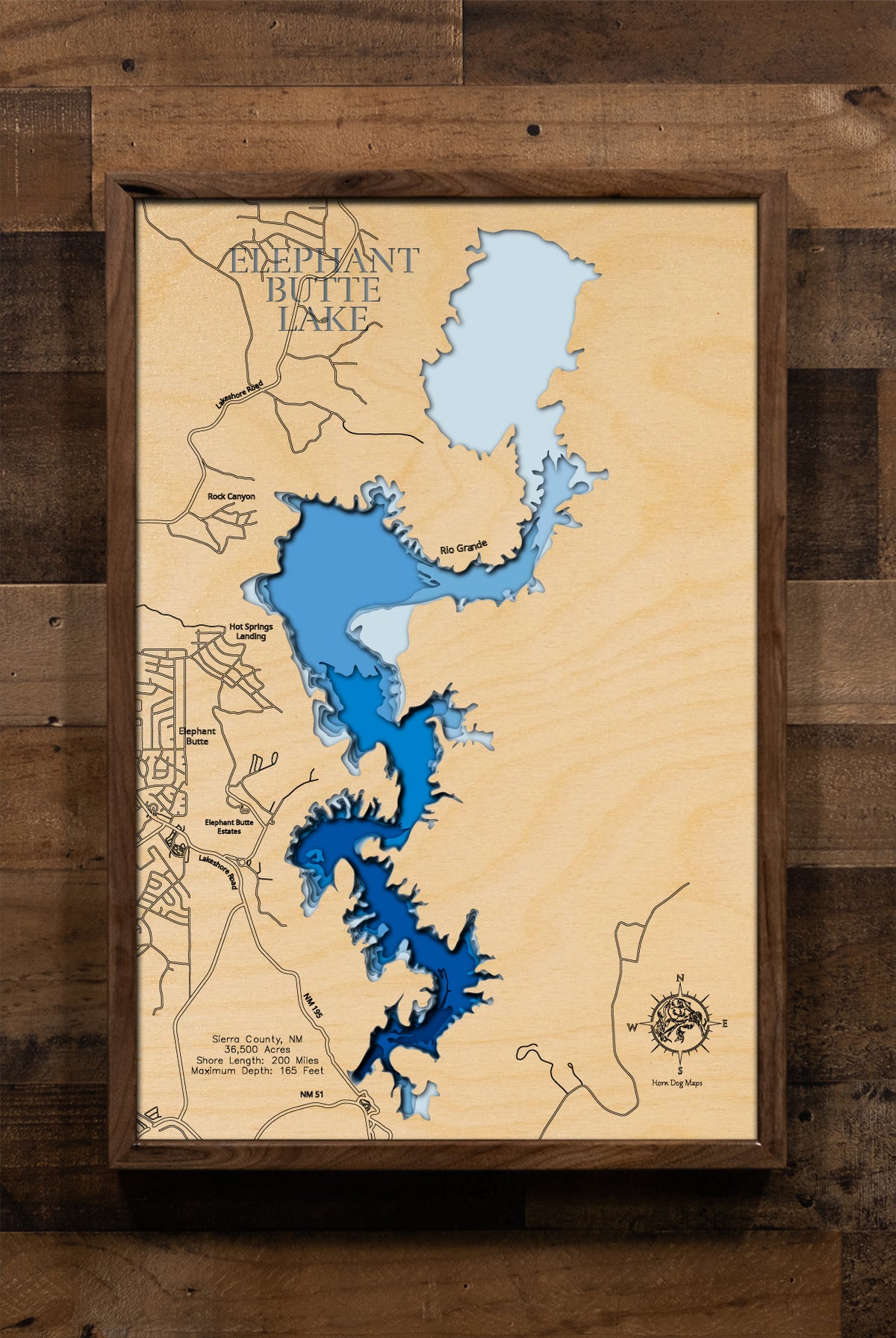 A laser-cut, layered wooden map of Elephant Butte Lake in Sierra County, New Mexico. The sprawling and irregular shape of this large reservoir, winding through the New Mexico landscape, is clearly visible. The varying depths of the lake, reaching a maximum of 165 feet, are represented by different layers of wood, illustrating its impressive underwater topography.