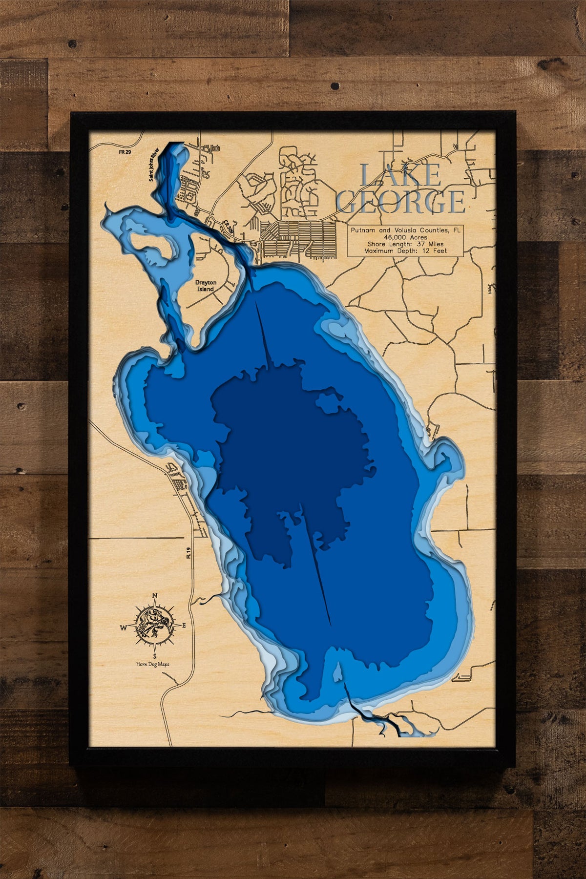 A laser-cut, layered wood map of Lake George, Florida, illustrating its expansive shape and forest-lined borders in Putnam and Volusia Counties.