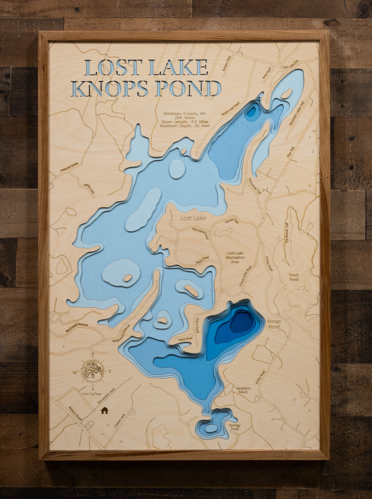 A highly detailed, laser-cut, and multi-layered wooden map of Lost Lake and Knops Pond in Groton, Middlesex County, Massachusetts. The map illustrates the 204-acre reservoir with its distinctive shallow northern Lost Lake basin and the deeper southern Knops Pond section featuring the 30-foot maximum depth, multiple scenic islands, and 4.5 miles of forested shoreline.
