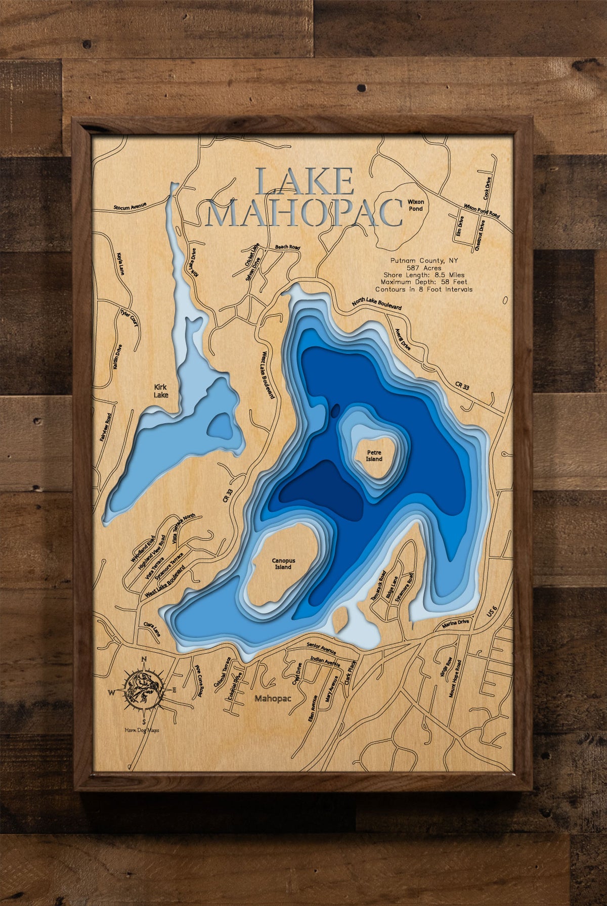 A laser-cut, layered wooden map of Lake Mahopac in Putnam County, New York. The distinct shape of this natural lake, with its 8.5-mile shoreline and numerous islands, is clearly visible within the forested landscape. The varying depths of the lake, reaching a maximum of 58 feet and detailed by 8-foot contour intervals, are represented by different layers of wood, illustrating its impressive underwater topography.