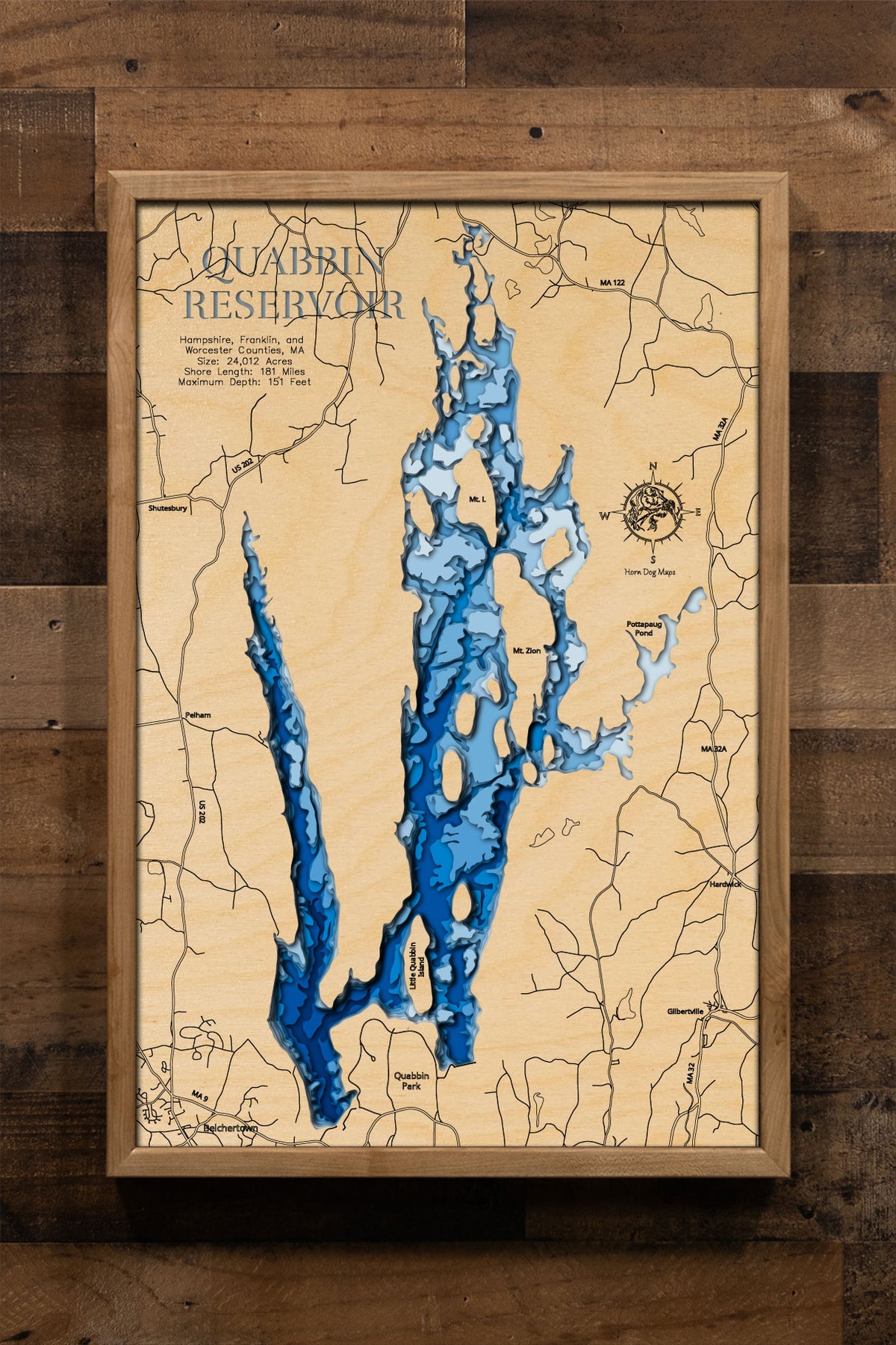 A laser-cut, layered wooden map of the Quabbin Reservoir, located in Hampshire, Franklin, and Worcester Counties, Massachusetts. The intricate and lengthy shoreline of this significant water body, with its many islands contributing to its unique shape, is clearly depicted in varying layers of wood to represent depth. The overall form of the reservoir within central Massachusetts is visually prominent.