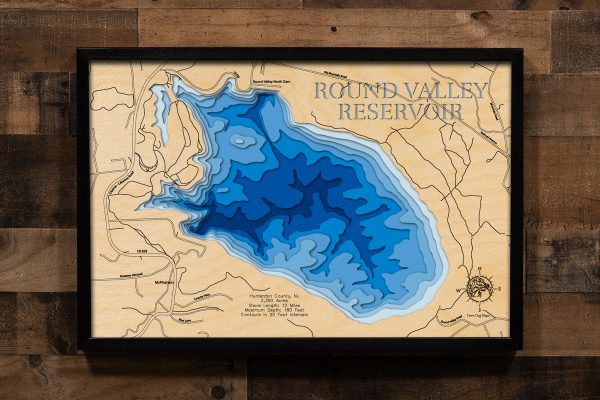 A laser-cut, layered wooden map of Round Valley Reservoir in Hunterdon County, New Jersey. The distinctive, almost circular shape of this deep reservoir, with its 12-mile shoreline, is clearly visible within the central New Jersey landscape. The varying depths of the lake, reaching a maximum of 180 feet and detailed by 20-foot contour intervals, are represented by different layers of wood, illustrating its impressive underwater topography.