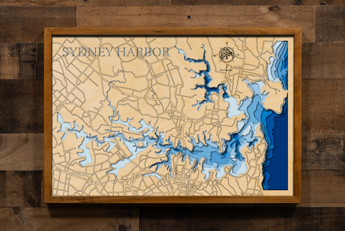 A laser-cut, layered wooden map of Sydney Harbour in New South Wales, Australia. The intricate and highly detailed shape of the harbour, with its numerous bays, coves, and islands, is clearly visible. Iconic structures like the Sydney Opera House and Sydney Harbour Bridge are subtly integrated into the design. The varying depths of the harbour, reaching a maximum of 154 feet, are represented by different layers of wood, illustrating its underwater topography.
