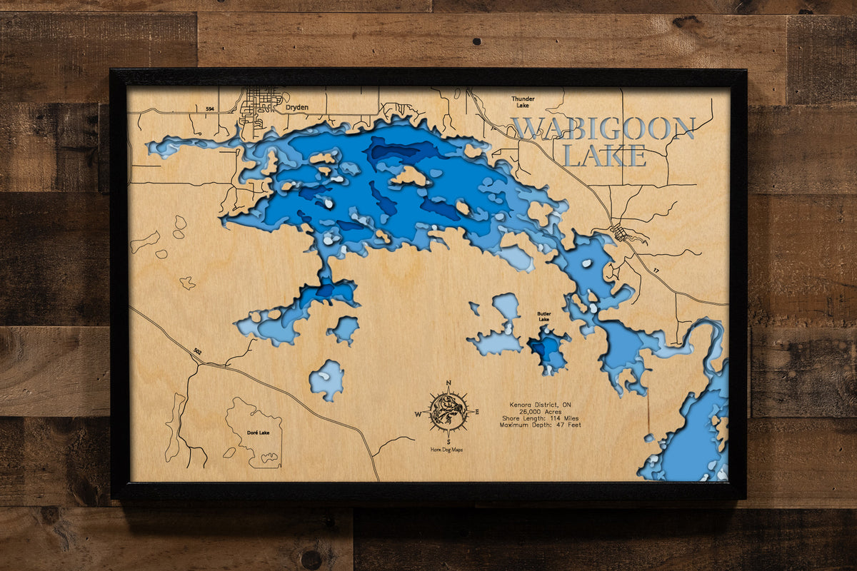 A magnificently detailed, laser-cut, multi-layered wooden topographical map of Wabigoon Lake in Kenora District, Ontario, Canada, showcasing the expansive 26,000-acre surface stretching 20 miles long with hundreds of islands and intricate 114 miles of shoreline. The natural wood top layer frames productive bays, the Wabigoon River connections, and the nine-lake chain system, while graduated blue layers create a stunning visual gradient from the 20-foot average depth to the 47-foot maximum depth.