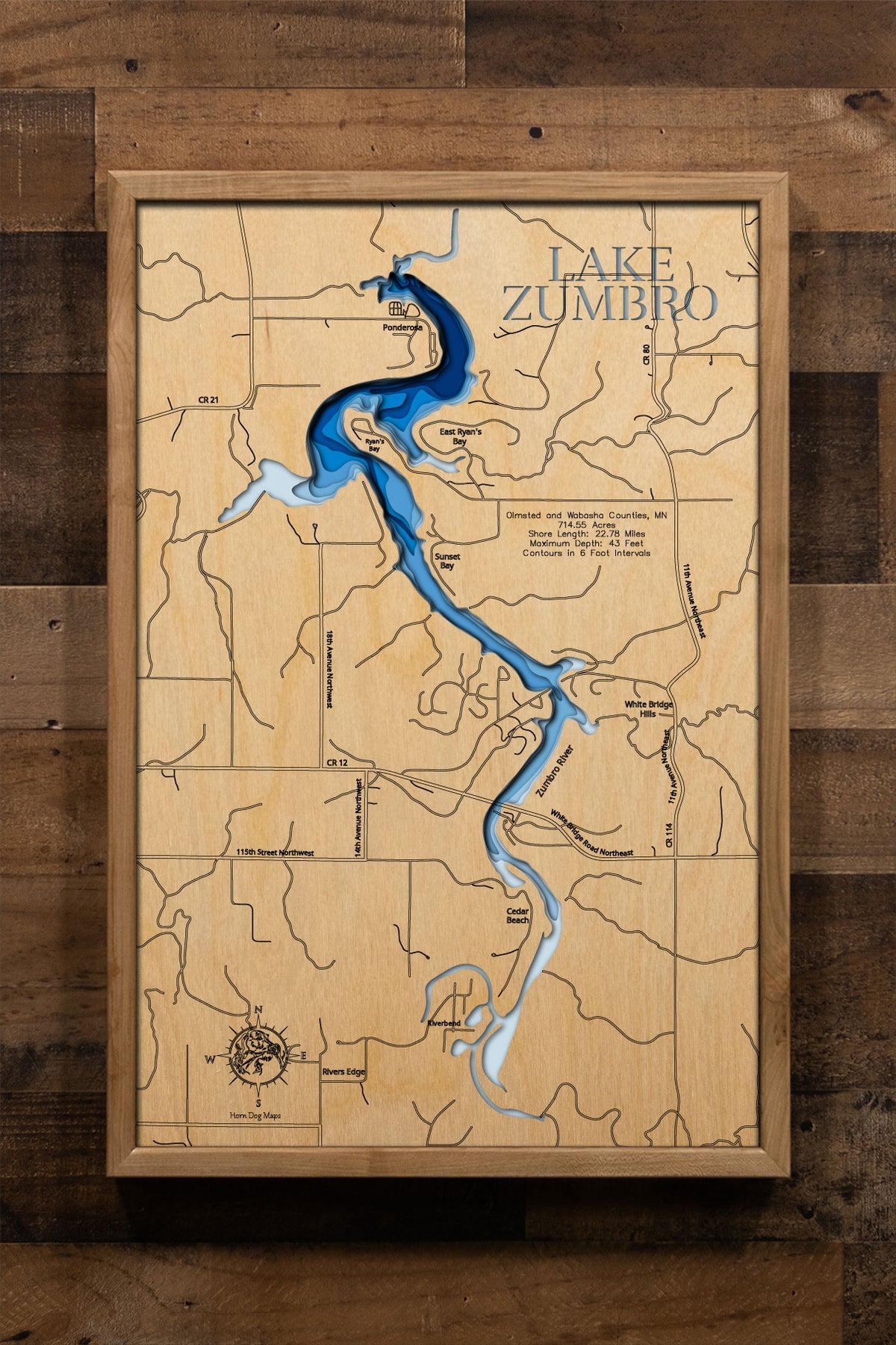 A laser-cut, layered wooden map of Lake Zumbro in Olmsted and Wabasha Counties, Minnesota. The distinct, elongated shape of this reservoir, with its 22.78-mile shoreline, is clearly visible as it winds through the bluffs of southeastern Minnesota. The varying depths of the lake, reaching a maximum of 43 feet and detailed by 6-foot contour intervals, are represented by different layers of wood, illustrating its impressive underwater topography.