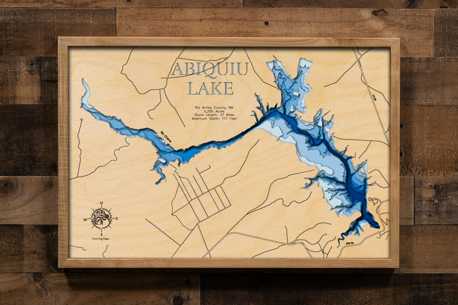 A laser-cut, layered wooden map of Abiquiu Lake in Rio Arriba County, New Mexico. The distinct shape of this pristine lake, with its 37-mile shoreline, is clearly visible within the northern New Mexico landscape. The varying depths of the lake, reaching a maximum of 117 feet, are represented by different layers of wood, illustrating its impressive underwater topography.
