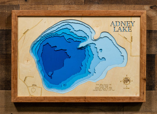 A framed 3D wooden depth map of Adney Lake, featuring layered blue wood sections representing different water depths on a light wood background, enclosed in a medium brown wooden frame and mounted on a dark wood wall.