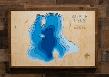 A laser-cut, layered wooden map of Agate Lake in Crow Wing County, Minnesota. The distinct shape of this natural lake, with its 2.63-mile shoreline, is clearly visible within the forested landscape of central Minnesota. The varying depths of the lake, reaching a maximum of 25 feet, are represented by different layers of wood, illustrating its impressive underwater topography.