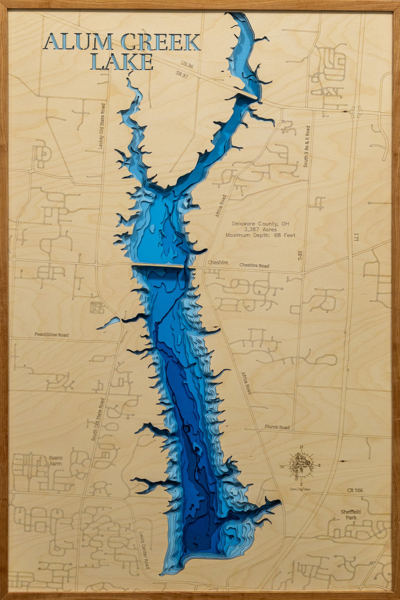 A detailed, laser-cut wooden map of Alum Creek Lake in Delaware County, Ohio, showcasing the reservoir's 3,387 acres and irregular shoreline. The map illustrates the division between the unlimited-horsepower southern basin and the quieter northern coves, with etched lines highlighting the maximum 68-foot depth near the dam structure.