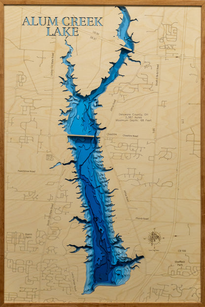 A detailed, laser-cut wooden map of Alum Creek Lake in Delaware County, Ohio, showcasing the reservoir's 3,387 acres and irregular shoreline. The map illustrates the division between the unlimited-horsepower southern basin and the quieter northern coves, with etched lines highlighting the maximum 68-foot depth near the dam structure.