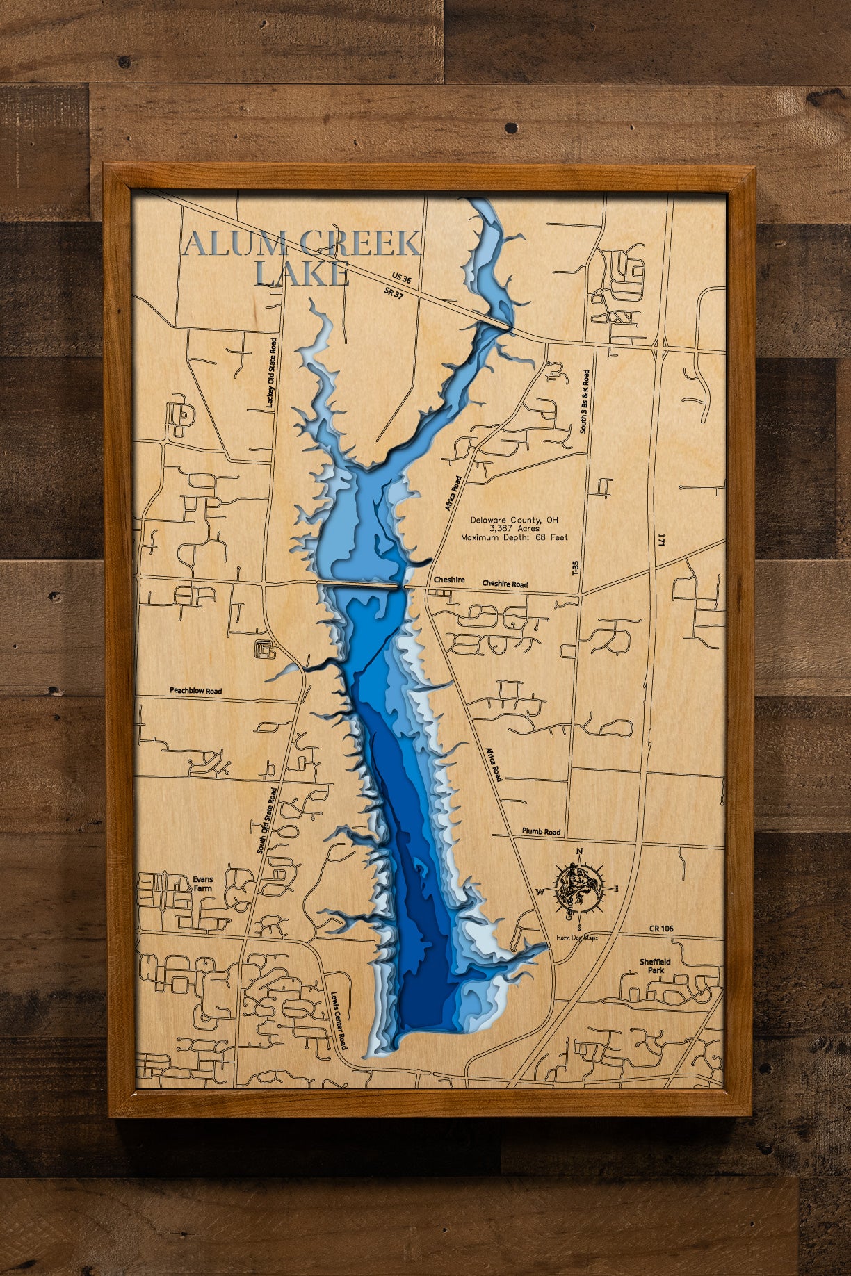 A detailed, laser-cut wooden map of Alum Creek Lake in Delaware County, Ohio, showcasing the reservoir's 3,387 acres and irregular shoreline. The map illustrates the division between the unlimited-horsepower southern basin and the quieter northern coves, with etched lines highlighting the maximum 68-foot depth near the dam structure.