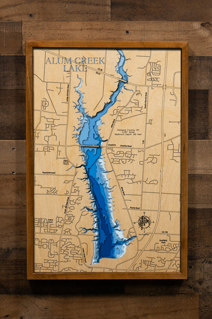 A detailed, laser-cut wooden map of Alum Creek Lake in Delaware County, Ohio, showcasing the reservoir's 3,387 acres and irregular shoreline. The map illustrates the division between the unlimited-horsepower southern basin and the quieter northern coves, with etched lines highlighting the maximum 68-foot depth near the dam structure.