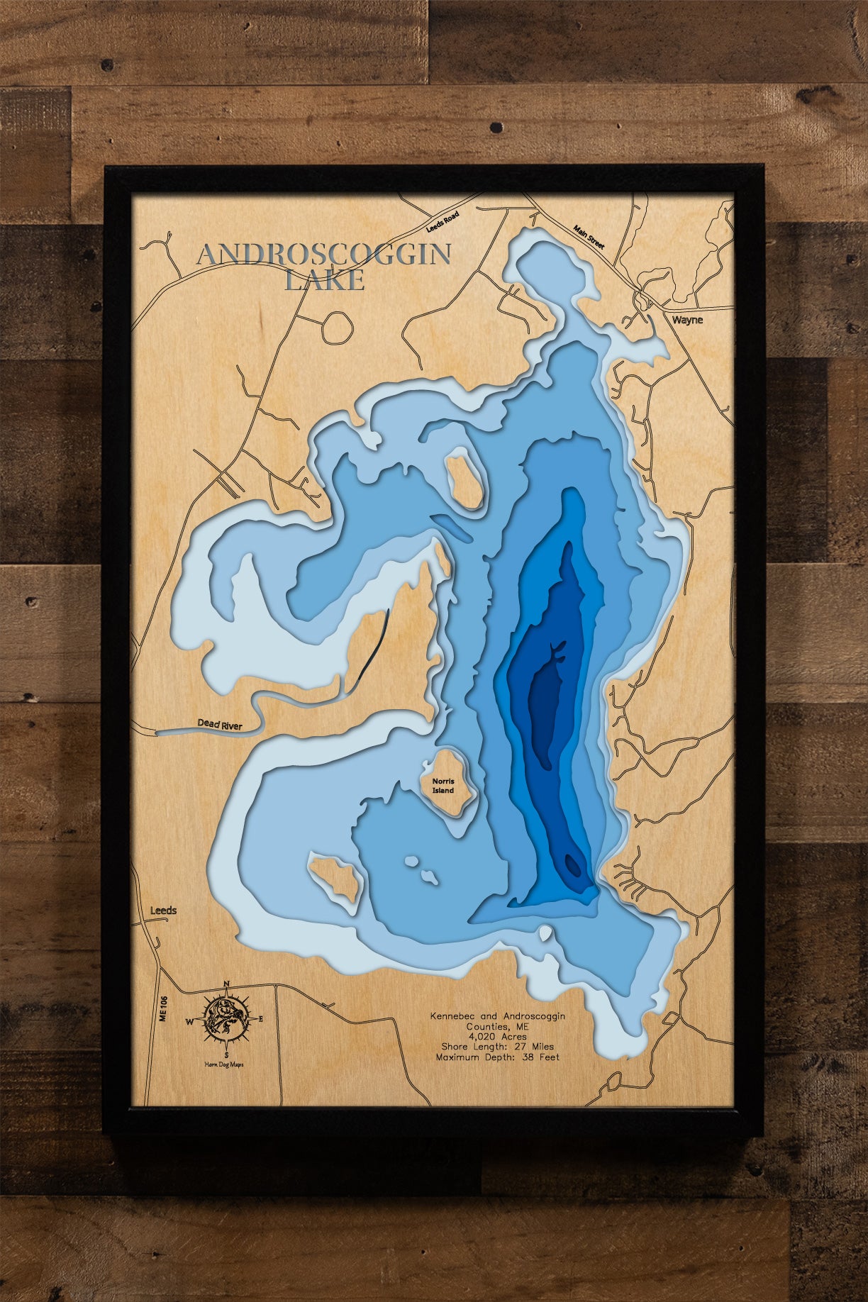A precision laser-cut, multi-layered wooden map of Androscoggin Lake in Kennebec and Androscoggin Counties, Maine. The natural wood top layer captures 27 miles of shoreline and four scenic islands in fine detail, while a light-to-dark blue gradient conveys the lake's shallow, warmwater character. A handcrafted statement piece for any Maine lake camp, cabin, or outdoor enthusiast's wall.