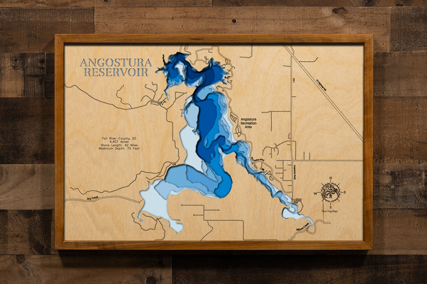 A beautifully detailed, laser-cut, multi-layered wooden topographical map of Angostura Reservoir in Fall River County, South Dakota, showcasing the 4,407-acre reservoir's expansive surface area with precise depth contours from shallow beaches to the impressive 75-foot maximum depth. The natural wood top layer frames 42 miles of intricate shoreline detail, while graduated blue layers create a striking visual gradient.