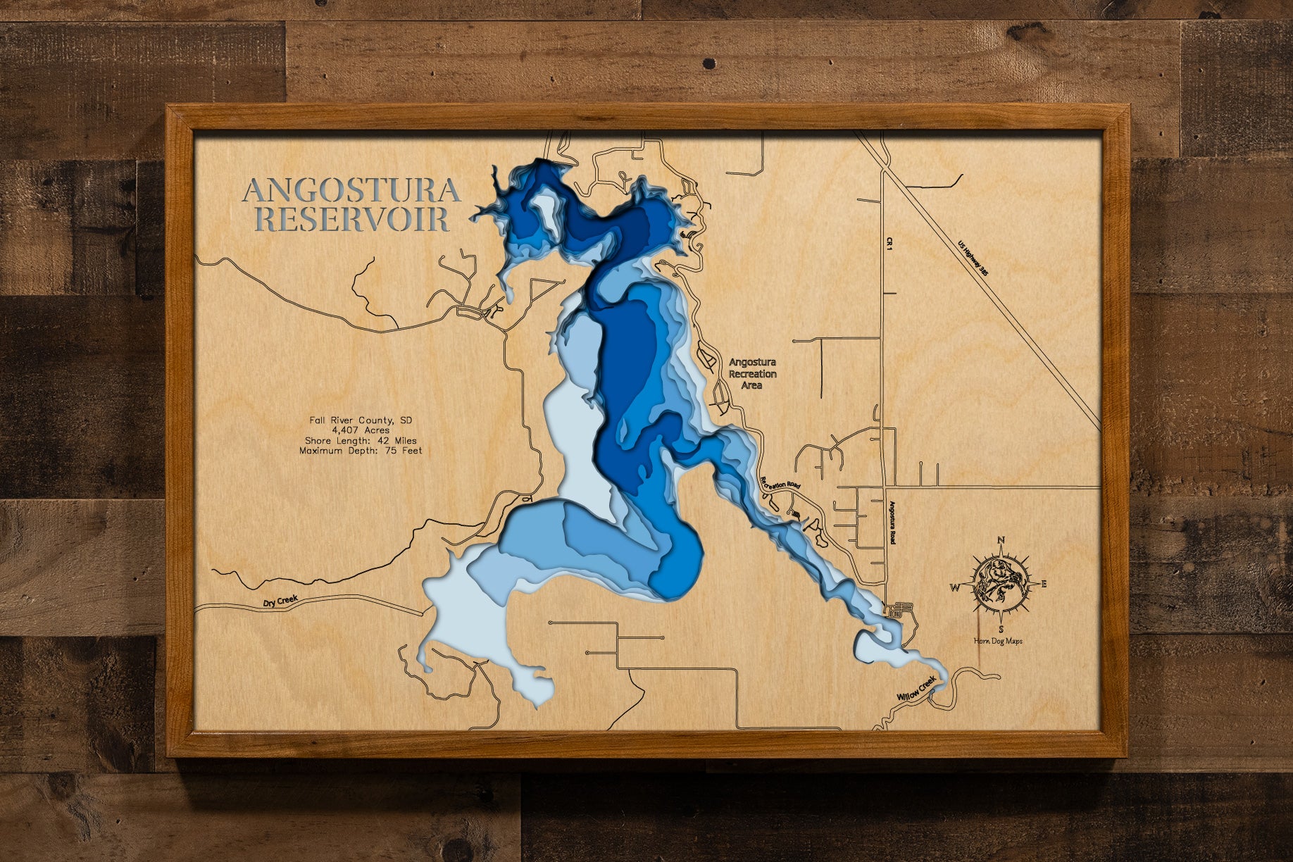 A beautifully detailed, laser-cut, multi-layered wooden topographical map of Angostura Reservoir in Fall River County, South Dakota, showcasing the 4,407-acre reservoir's expansive surface area with precise depth contours from shallow beaches to the impressive 75-foot maximum depth. The natural wood top layer frames 42 miles of intricate shoreline detail, while graduated blue layers create a striking visual gradient.