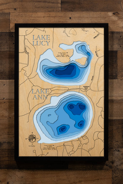 A precision laser-cut, multi-layered wooden map of Lake Ann and Lake Lucy in Carver County, Minnesota — two connected Chanhassen lakes linked by Riley Creek, spanning 119 and 88 acres respectively. The natural wood top layer captures both shorelines and their connecting waterway in fine detail, while a light-to-dark blue gradient conveys their depth and clean character. A handcrafted statement piece for any Minnesota lake home, cabin, or Twin Cities enthusiast's wall.