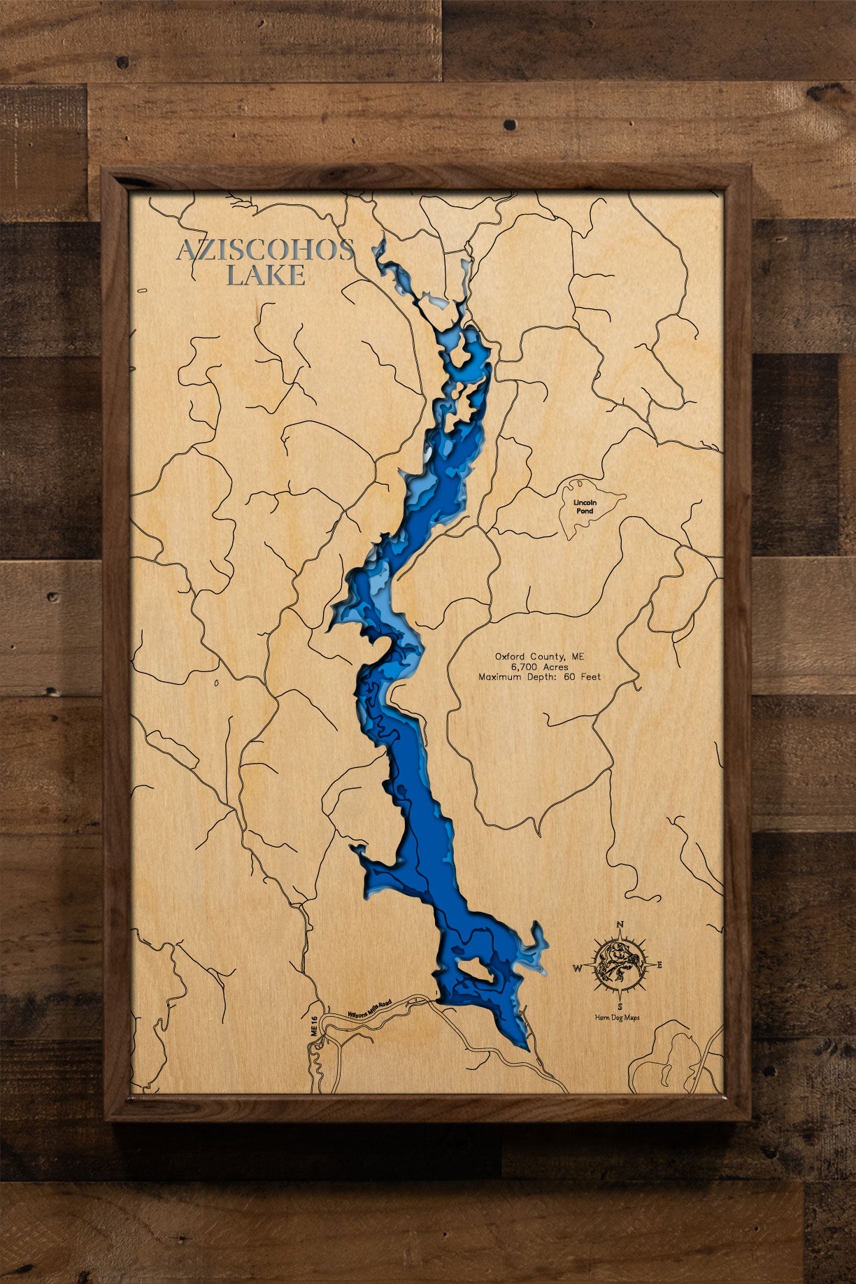 A precision laser-cut, multi-layered wooden map of Aziscohos Lake in Oxford County, Maine, a 6,700-acre Magalloway River reservoir near the New Hampshire border known for its prized Landlocked Salmon and Brook Trout fishery. The natural wood top layer captures the lake's wild, undeveloped shoreline in fine detail, while a light-to-dark blue gradient conveys its 60-foot depth. A handcrafted statement piece for any Maine camp, western wilderness retreat, or outdoor enthusiast's wall.