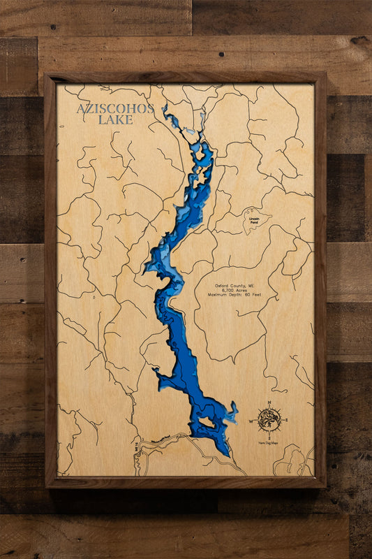 A precision laser-cut, multi-layered wooden map of Aziscohos Lake in Oxford County, Maine, a 6,700-acre Magalloway River reservoir near the New Hampshire border known for its prized Landlocked Salmon and Brook Trout fishery. The natural wood top layer captures the lake's wild, undeveloped shoreline in fine detail, while a light-to-dark blue gradient conveys its 60-foot depth. A handcrafted statement piece for any Maine camp, western wilderness retreat, or outdoor enthusiast's wall.