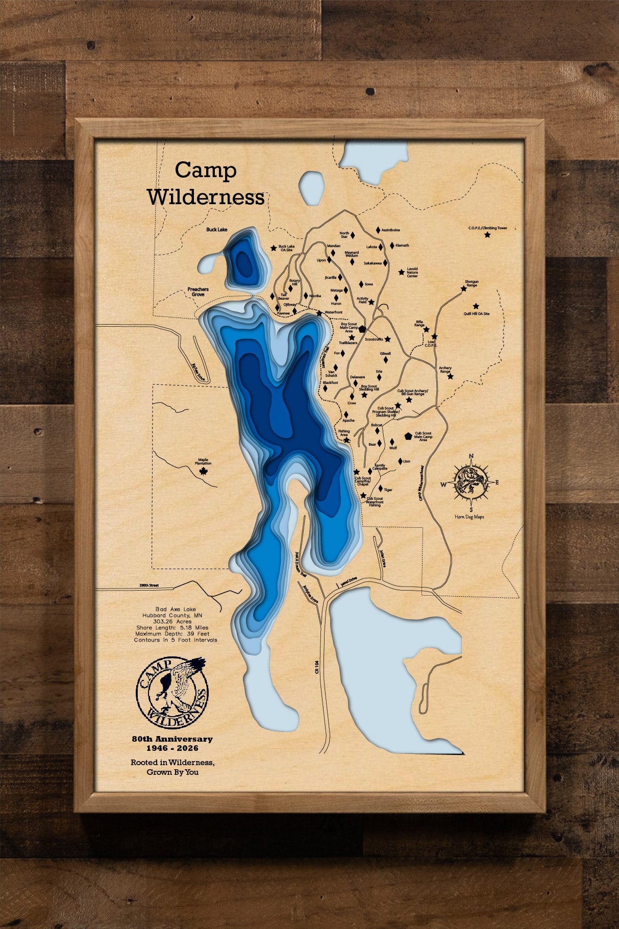 A precision laser-cut, multi-layered wooden map of Bad Axe Lake in Hubbard County, Minnesota — home to the legendary Camp Wilderness Scout Camp. The natural wood top layer traces the lake's pristine, protected shoreline in fine detail, while a light-to-dark blue gradient highlights the water's depth and dimension. A meaningful and rustic statement piece for a lodge, troop room, or Scout family home.