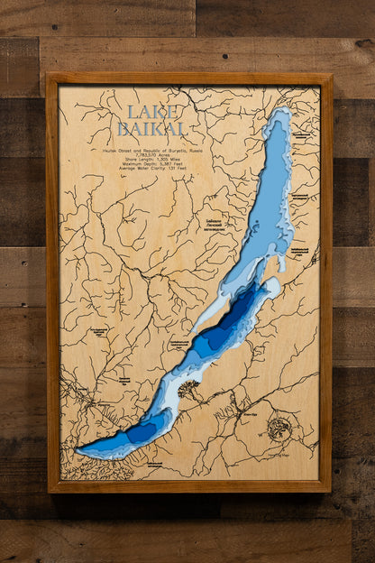 A breathtakingly detailed, laser-cut, multi-layered wooden map of Lake Baikal in southern Siberia, Russia, showcasing the world's deepest and oldest lake spanning 7.8 million acres with its distinctive 395-mile crescent shape. The topographic design features natural wood layers highlighting the 1,305 miles of mountainous shoreline, 27 islands including Olkhon, and graduated blue water layers illustrating the extraordinary depths to 5,387 feet.