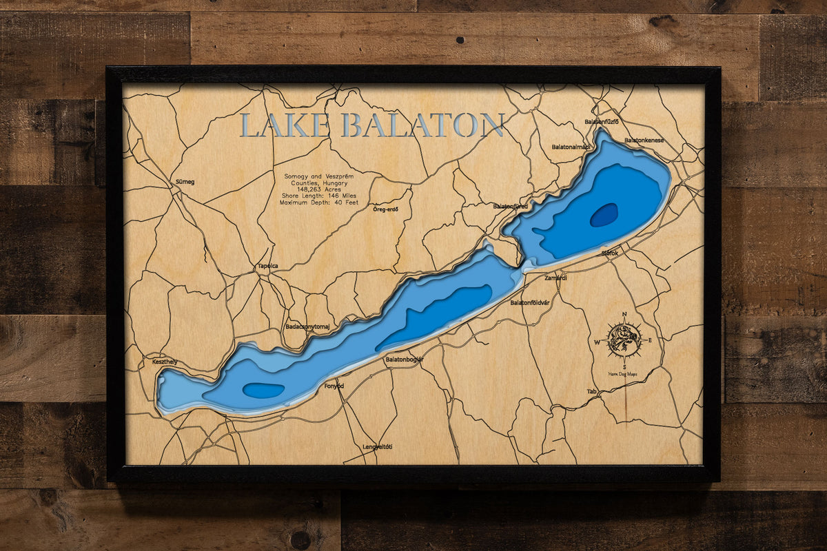 A precision laser-cut, multi-layered wooden map of Lake Balaton in Hungary, the largest lake in Central Europe at 148,263 acres with 146 miles of shoreline stretching 48 miles across Somogy and Veszprém Counties. The natural wood top layer captures the lake's dramatic elongated form and the Tihany Peninsula in fine detail, while a light-to-dark blue gradient conveys its shallow, sun-warmed character. A handcrafted statement piece for any European lake home, Hungarian retreat, or world traveler's wall.