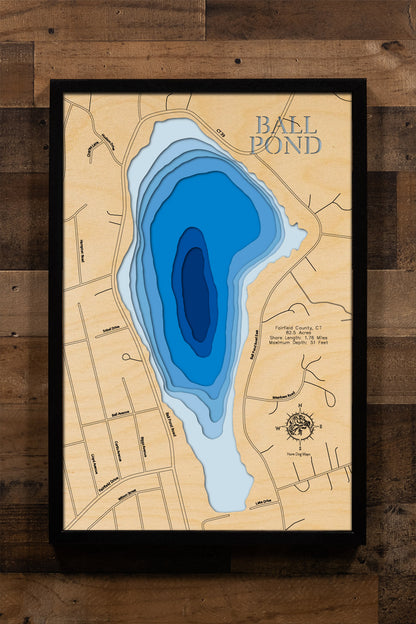 A laser-cut, layered wooden map of Ball Pond in Fairfield County, Connecticut. The distinct shape of this natural lake, with its 1.76-mile shoreline, is clearly visible within the landscape of New Fairfield. The varying depths of the lake, reaching a maximum of 51 feet, are represented by different layers of wood, illustrating its underwater topography.
