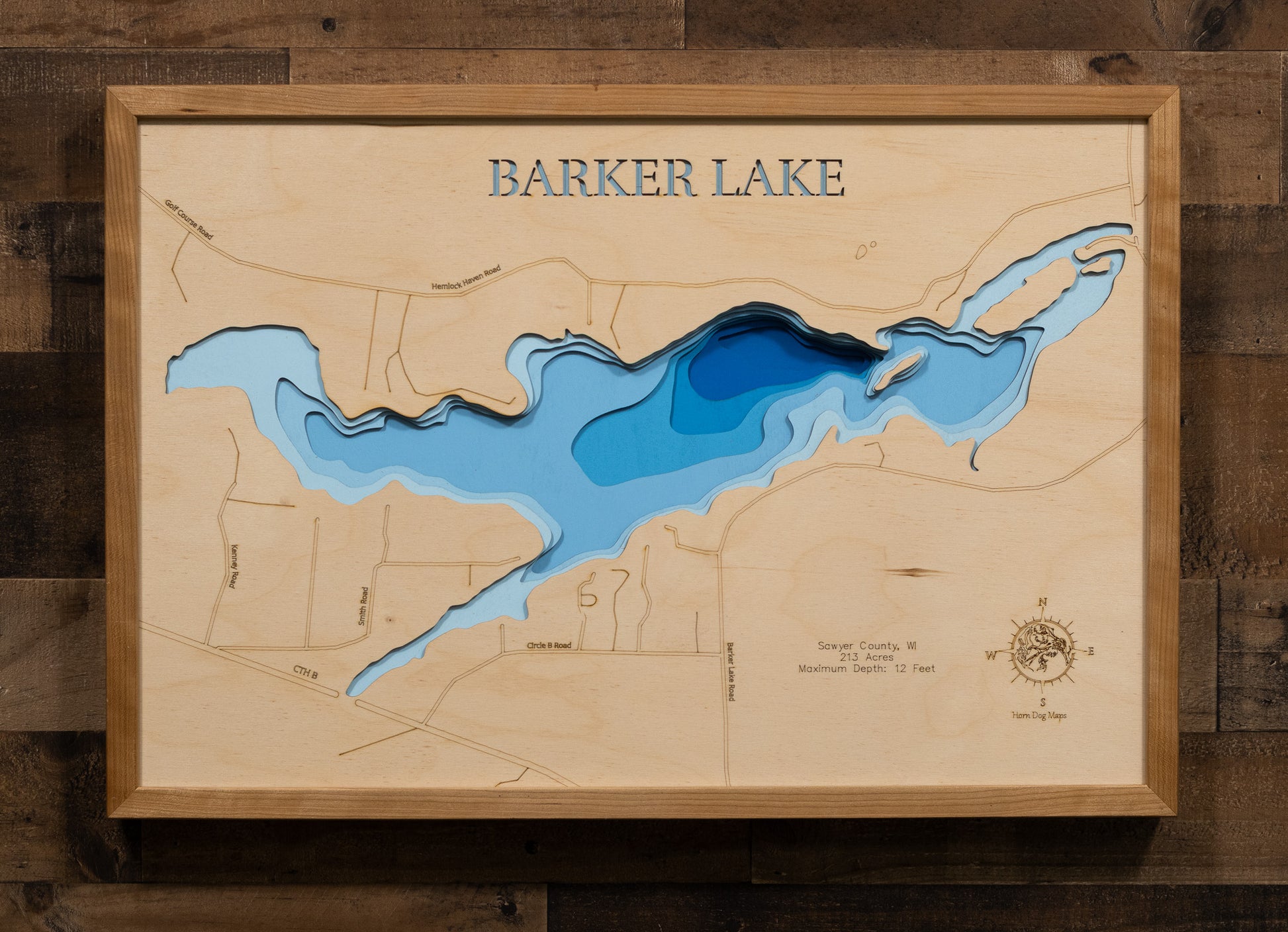 A laser-cut, layered wooden map of Barker Lake in Sawyer County, Wisconsin. The shape of the lake is visible within the northwestern Wisconsin landscape. The varying depths of the lake, reaching a maximum of 12 feet, are represented by different layers of wood.