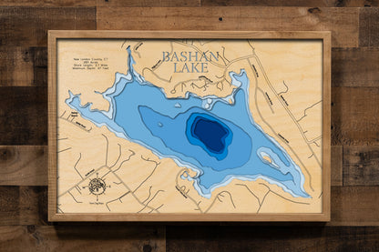 A laser-cut, layered wooden map of Bashan Lake in New London County, Connecticut. The distinct shape of this natural lake, with its 3.7-mile shoreline, is clearly visible within the landscape of East Haddam. The varying depths of the lake, reaching a maximum of 60 feet, are represented by different layers of wood, illustrating its impressive underwater topography.
