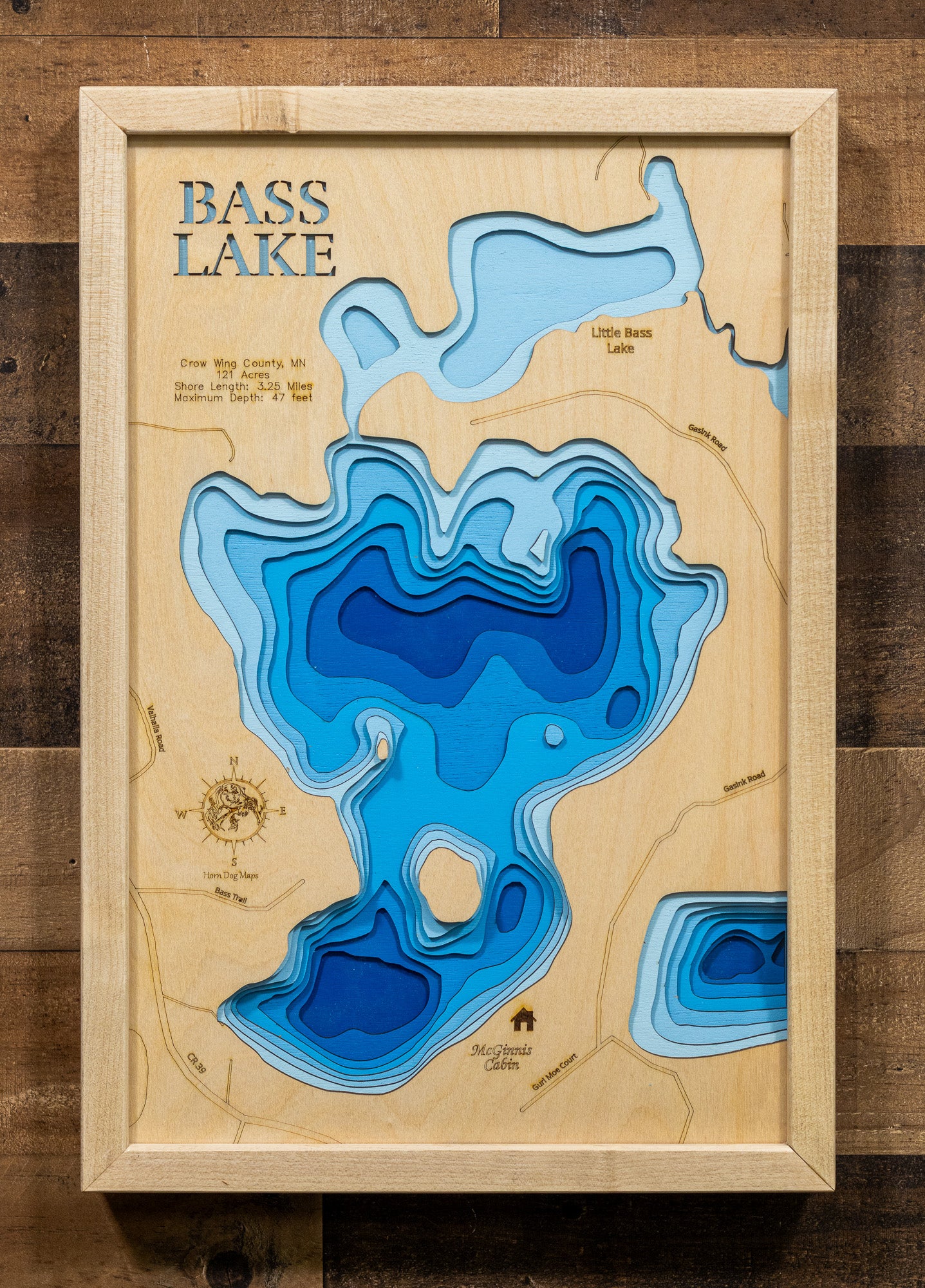A custom-engraved, laser-cut wooden lake map of Bass Lake in Crow Wing County, Minnesota. The map highlights the lake's accurate shape and detailed 3.25-mile shoreline, with its basin and maximum depth of 47 feet represented by a deep blue stain. The design includes elegantly etched details of the lake's unique shape and surrounding features, providing a detailed, informative guide to this popular Minnesota lake.