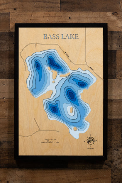 A precision laser-cut, multi-layered wooden map of Bass Lake in Rusk County, Wisconsin, an 83-acre Northwoods lake near Strickland holding Musky, Walleye, Trout, Bass, and Pike. The natural wood top layer captures the lake's natural shoreline in fine detail, while a light-to-dark blue gradient conveys its 27-foot depth. A handcrafted statement piece for any Wisconsin lake cabin, home, or outdoor enthusiast's wall.