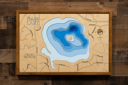 A highly detailed, laser-cut, and multi-layered wooden map of Bass Lake, a natural lake in Hennepin County, Minnesota. The map shows the lake's distinct shape and its 3.09-mile shoreline, highlighting its location within the suburban area of Plymouth. The varying depths of the lake, reaching a maximum of 34 feet, are represented by different layers of wood.