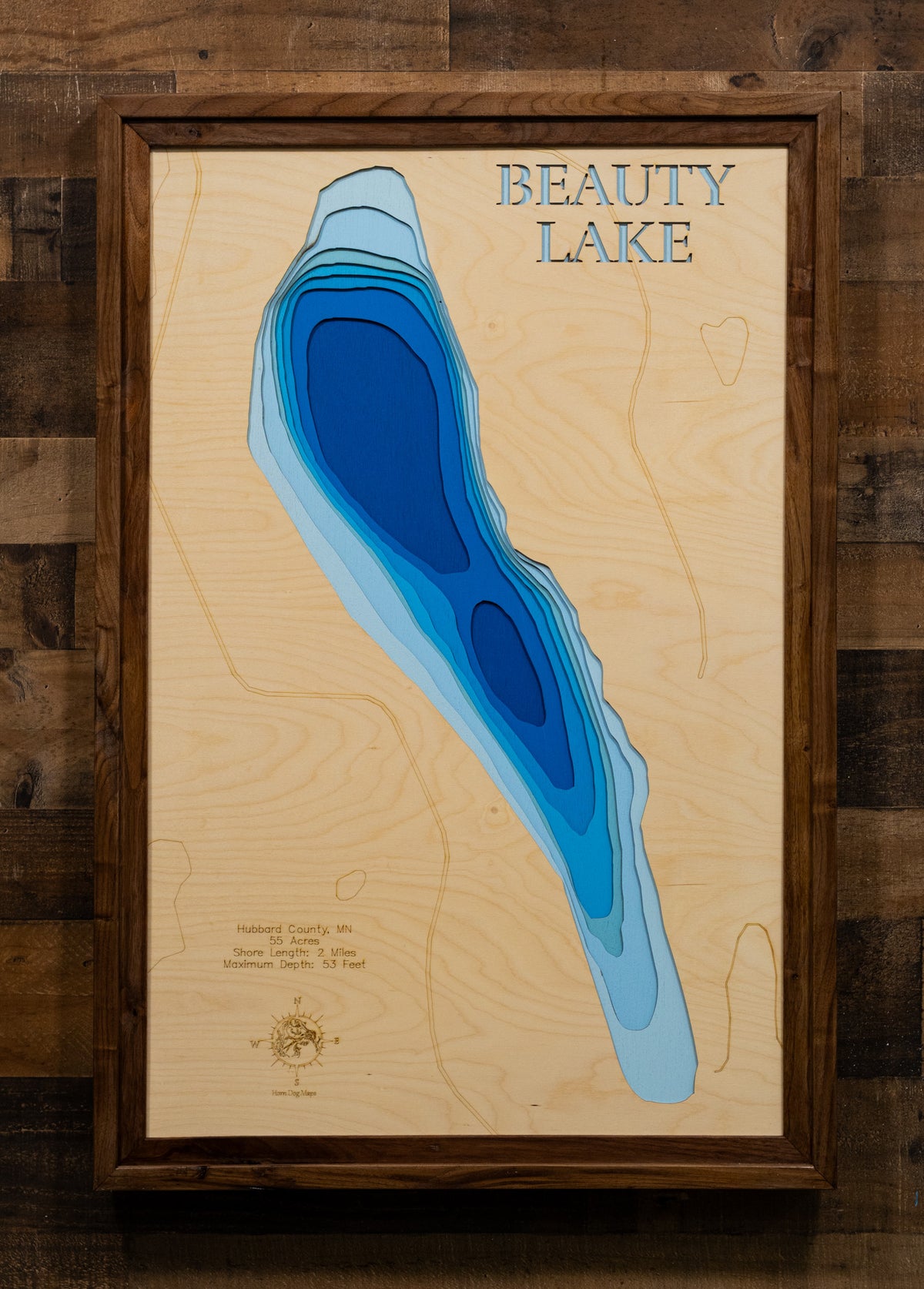 A precision laser-cut, multi-layered wooden map of Beauty Lake in Hubbard County, Minnesota — a pristine 55-acre clear-water lake 19 miles north of Park Rapids with a surprising maximum depth of 53 feet. The natural wood top layer captures 2 miles of pine-fringed shoreline in fine detail, while a light-to-dark blue gradient conveys the lake's remarkable depth and clarity. A handcrafted statement piece for any Minnesota Northwoods cabin, lake home, or outdoor enthusiast's wall.