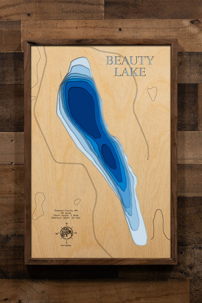 A precision laser-cut, multi-layered wooden map of Beauty Lake in Hubbard County, Minnesota — a pristine 55-acre clear-water lake 19 miles north of Park Rapids with a surprising maximum depth of 53 feet. The natural wood top layer captures 2 miles of pine-fringed shoreline in fine detail, while a light-to-dark blue gradient conveys the lake's remarkable depth and clarity. A handcrafted statement piece for any Minnesota Northwoods cabin, lake home, or outdoor enthusiast's wall.