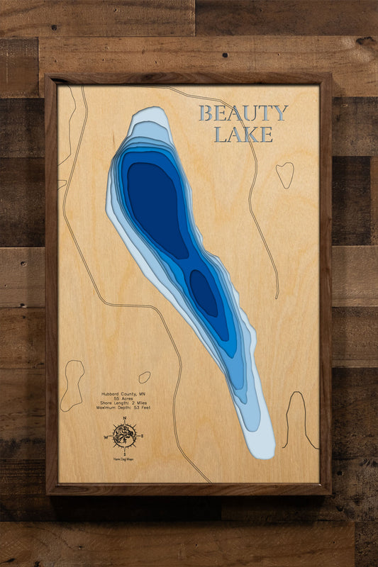 A precision laser-cut, multi-layered wooden map of Beauty Lake in Hubbard County, Minnesota — a pristine 55-acre clear-water lake 19 miles north of Park Rapids with a surprising maximum depth of 53 feet. The natural wood top layer captures 2 miles of pine-fringed shoreline in fine detail, while a light-to-dark blue gradient conveys the lake's remarkable depth and clarity. A handcrafted statement piece for any Minnesota Northwoods cabin, lake home, or outdoor enthusiast's wall.