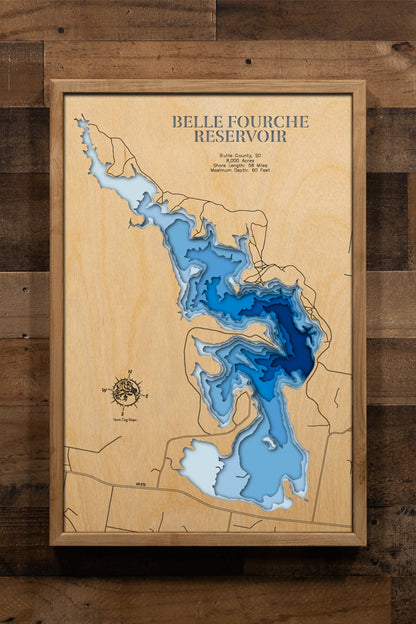 A meticulously crafted, laser-cut wooden topographic map of Belle Fourche Reservoir in Butte County, South Dakota, featuring multiple stacked layers that reveal the reservoir's 8,000-acre expanse and depth contours ranging from shallow shoreline areas to the 60-foot maximum depth near Orman Dam, with intricate details showing the 58 miles of winding shoreline, Owl Creek inlet, Rocky Point Recreation Area.