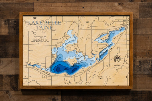 A highly detailed, 3D laser-cut wooden map of Lake Belle Taine in Hubbard County, Minnesota. The multi-layered design uses different wood tones to illustrate the lake's bathymetric contours and deepest points. Etched details include the lake name, county lines, shoreline roads, and the surrounding towns like Nevis, creating a unique and intricate piece of art.