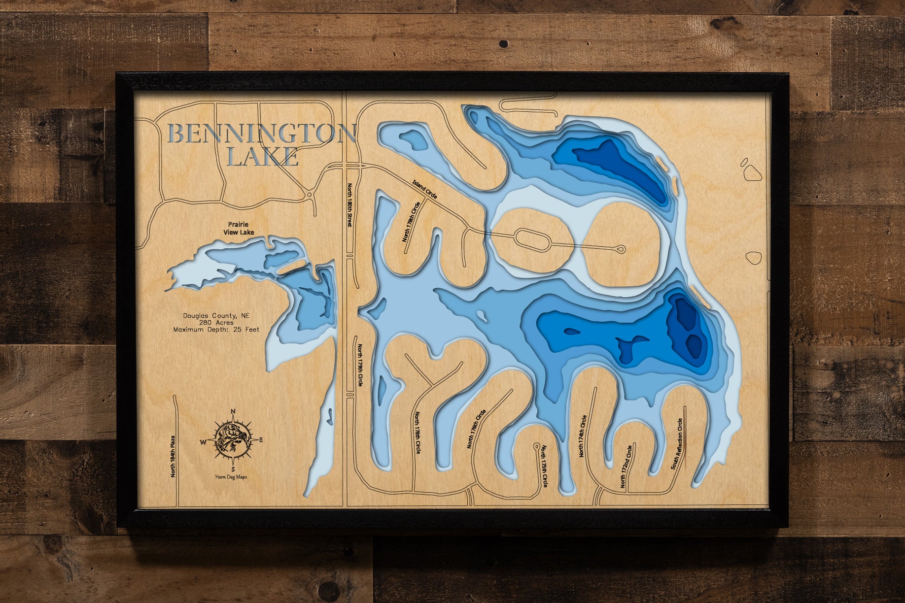 A precision laser-cut, multi-layered wooden map of Bennington Lake in Douglas County, Nebraska, a spring-fed residential lake just northwest of Omaha featuring scenic coves and two islands. The natural wood top layer captures the lake's clear, sandy-bottomed shoreline in fine detail, while a light-to-dark blue gradient brings its calm, community-centered waters to life. A handcrafted statement piece for any Nebraska lake home, cabin, or outdoor enthusiast's wall.
