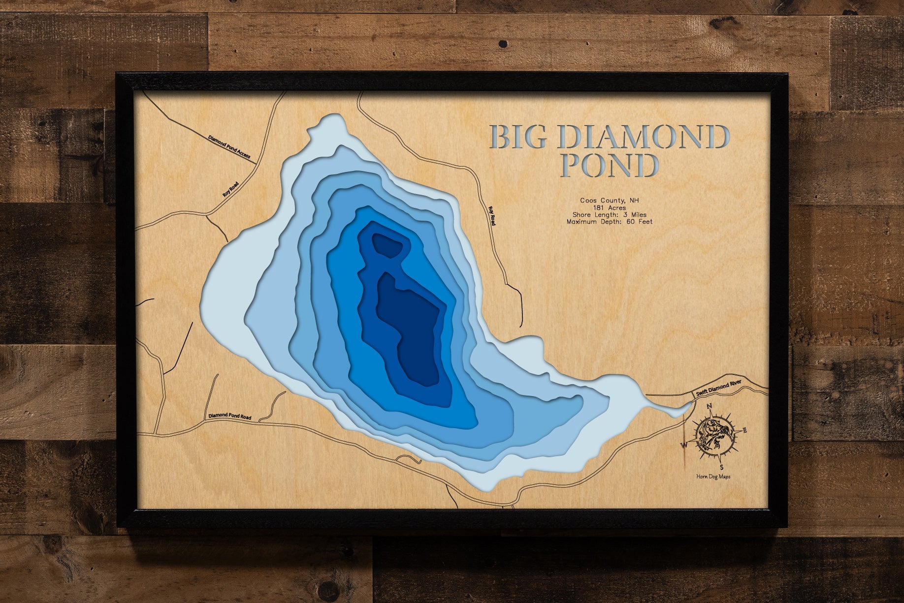 A magnificently detailed, laser-cut, multi-layered wooden topographical map of Big Diamond Pond in Coos County, New Hampshire, showcasing the pristine 181-acre glacial lake at 2,188 feet elevation with depth contours from shallow areas to the 60-foot maximum depth where the state record 37.65-pound Lake Trout was caught. The natural wood top layer frames approximately three miles of entirely undeveloped wilderness shoreline near the Canadian border, while graduated blue layers create a stunning visual depth