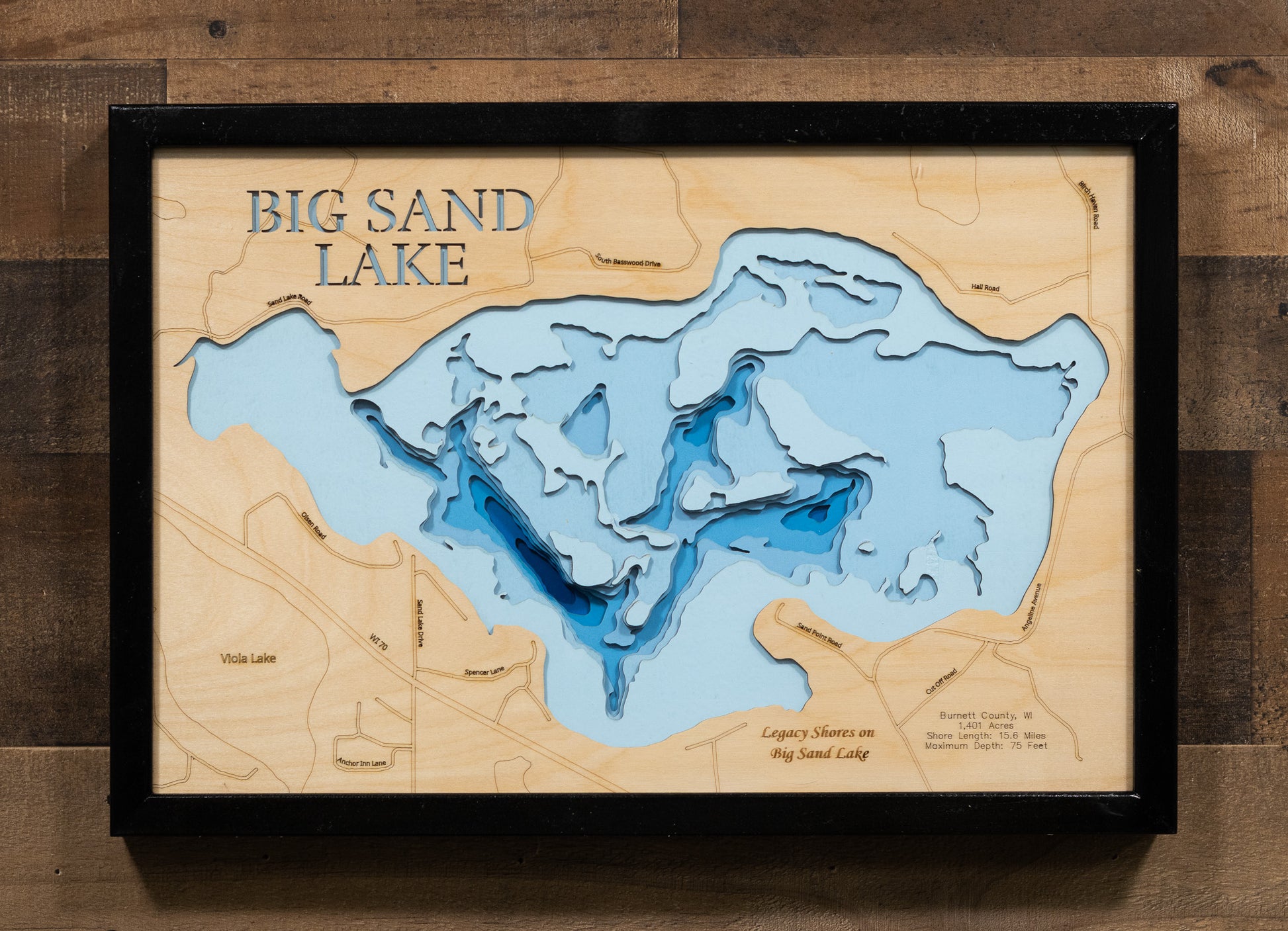 A laser-cut, layered wooden map of Big Sand Lake in Burnett County, Wisconsin. The shape of this significant natural lake, with its extensive shoreline, is visible within the northern Wisconsin landscape. The varying depths of the lake, reaching a maximum of 75 feet, are represented by different layers of wood, illustrating its underwater topography.