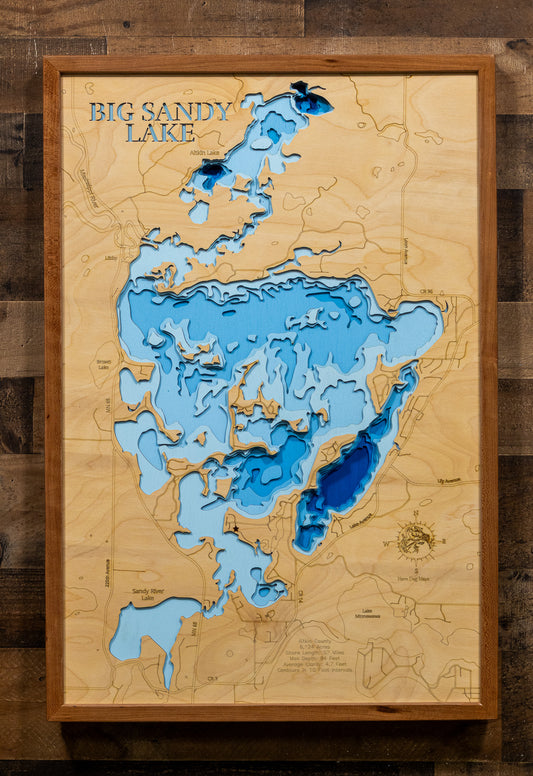 A framed 3D wooden depth map of Big Sandy Lake, featuring layered wood sections in light and dark blue to represent water depth, mounted on a rustic dark wood wall.