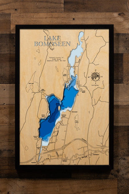 A finely detailed, multi-layered laser-cut wooden topographic map of Lake Bomoseen in Rutland County, Vermont, featuring depth contours illustrating the 65-foot maximum depth, the 2,400-acre glacially-carved basin with Neshobe Island prominently displayed in the center, Bomoseen State Park along the western shore with its distinctive quarry sites, the five major inlet streams, and the surrounding Taconic Mountain landscape that makes this Vermont's largest entirely in-state lake.