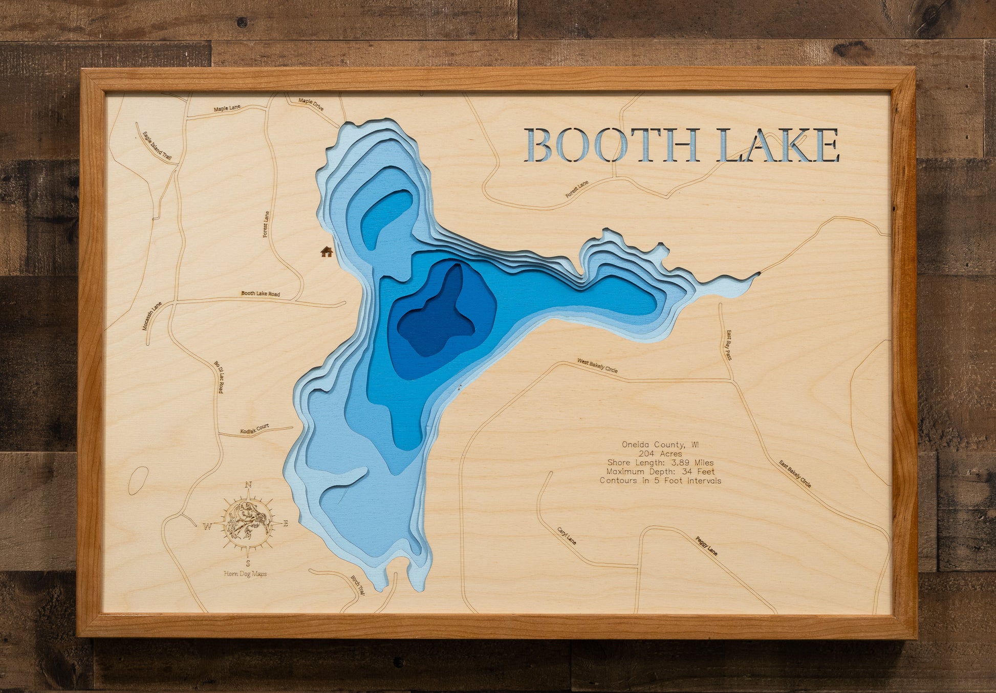 A highly detailed, laser-cut, and multi-layered wooden map of Booth Lake, a natural lake in Oneida County, Wisconsin. The map shows the lake's distinct shape, its 2.24-mile shoreline, and the surrounding natural area. The varying depths of the lake, reaching a maximum of 34 feet, are represented by different layers of wood.