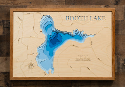 A highly detailed, laser-cut, and multi-layered wooden map of Booth Lake, a natural lake in Oneida County, Wisconsin. The map shows the lake's distinct shape, its 2.24-mile shoreline, and the surrounding natural area. The varying depths of the lake, reaching a maximum of 34 feet, are represented by different layers of wood.