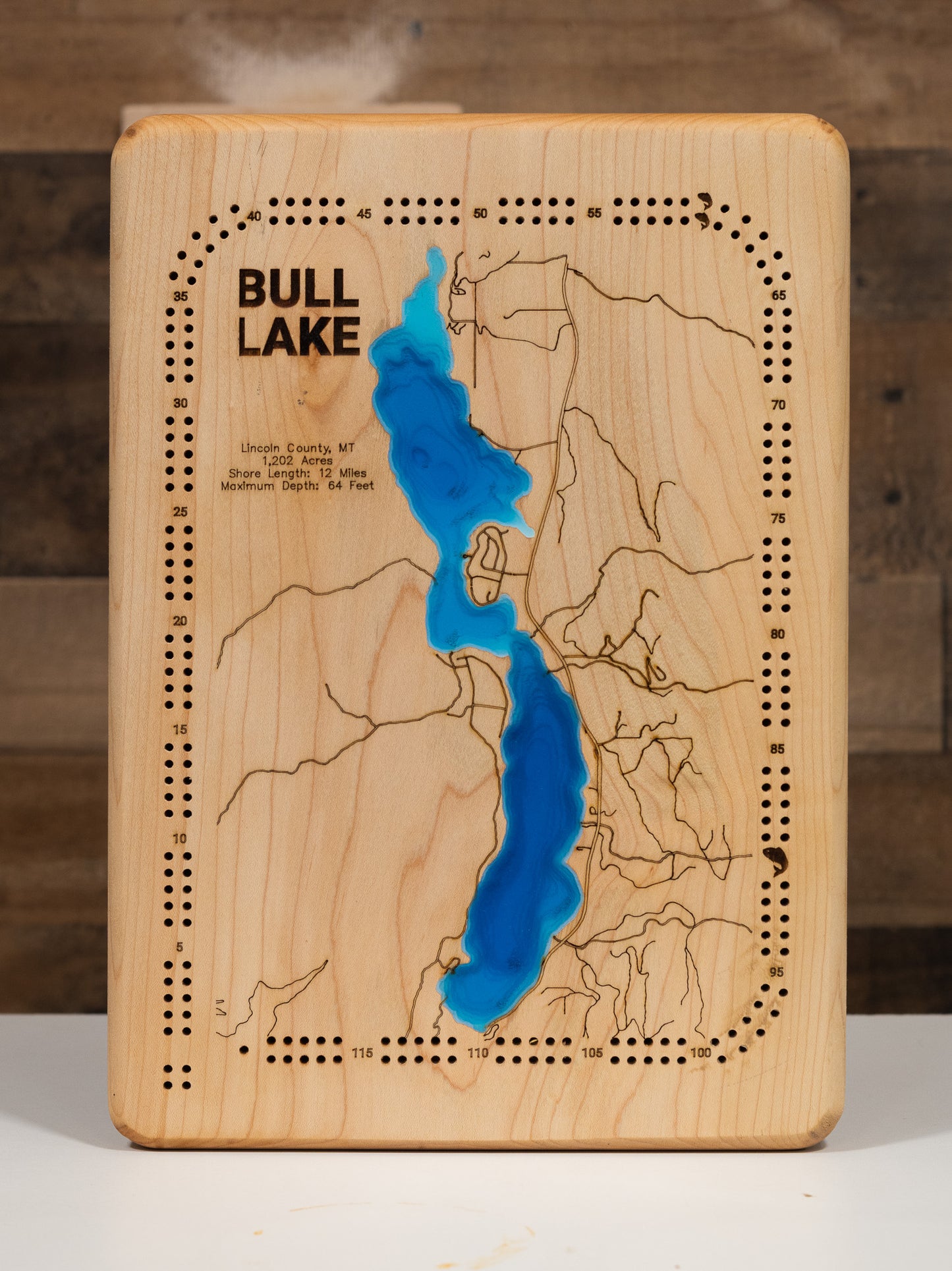 County, Montana, nestled in the Cabinet Mountains foothills, showcasing the 1,202-acre pristine mountain lake's 12 miles of forested shoreline, depth contours revealing the 64-foot maximum depth, and Montana Highway 56 running along the eastern shore.