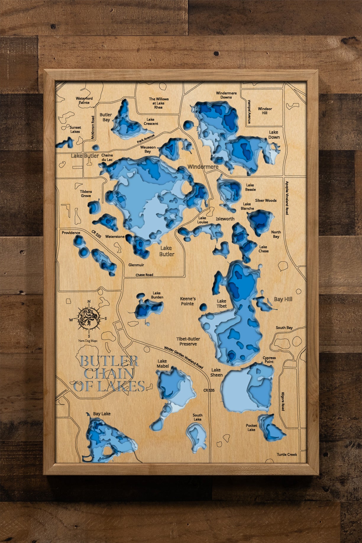 A precision laser-cut, multi-layered wooden map of the Butler Chain of Lakes in Orange County, Florida, capturing all 13 interconnected lakes and 32 connecting canals in striking detail. The natural wood top layer traces this iconic Central Florida chain, while a light-to-dark blue gradient conveys depths reaching 40 feet. A handcrafted statement piece for any Florida lakefront home or outdoor enthusiast's wall.
