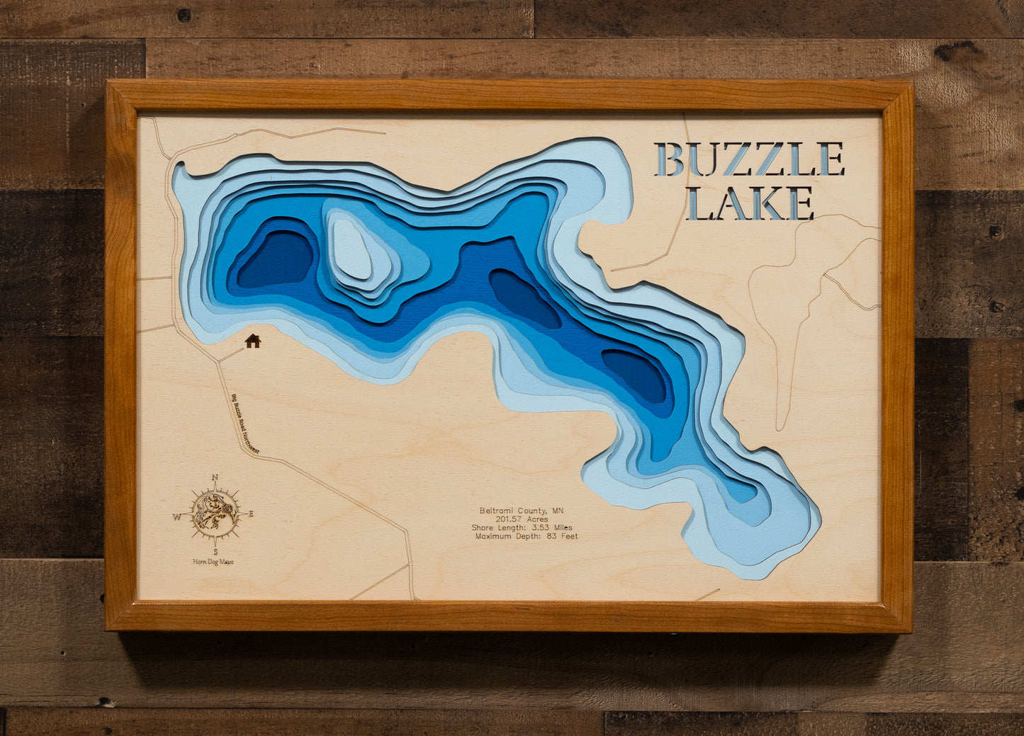 A laser-cut, layered wooden map of Buzzle Lake in Beltrami County, Minnesota. The shape of the lake is clearly defined within the northern Minnesota landscape. The varying depths of the lake, reaching a maximum of 83 feet, are represented by different layers of wood.